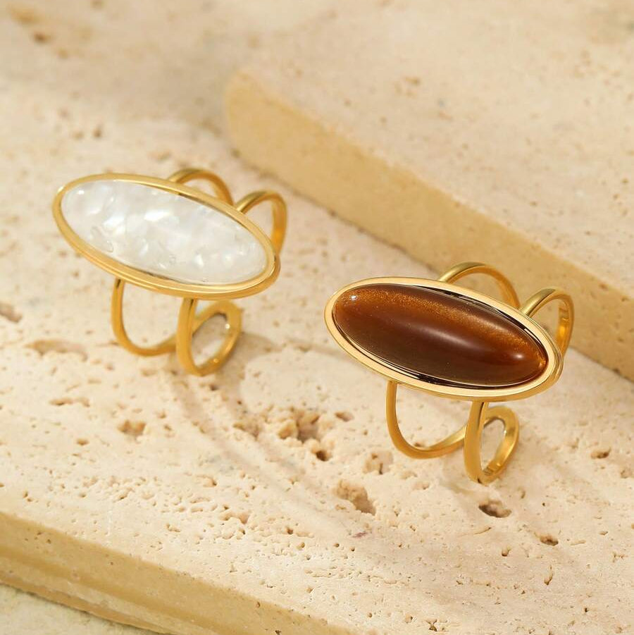 Two gold-rimmed rings with stone inlays on a beige surface