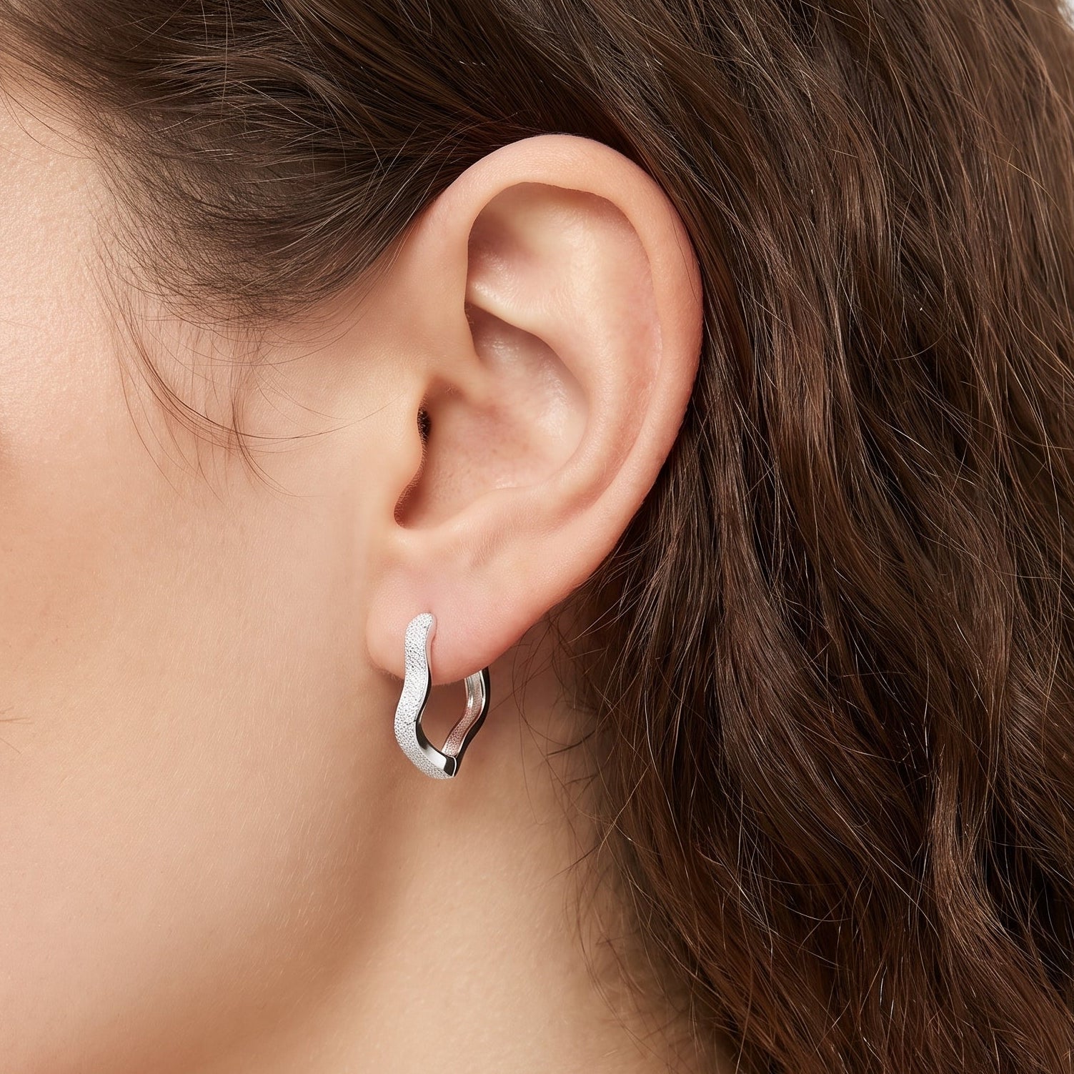 Silver frosted wavy huggie earring on the earlobe, close-up