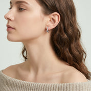 Silver frosted huggie earring in side profile with an oatmeal sweater