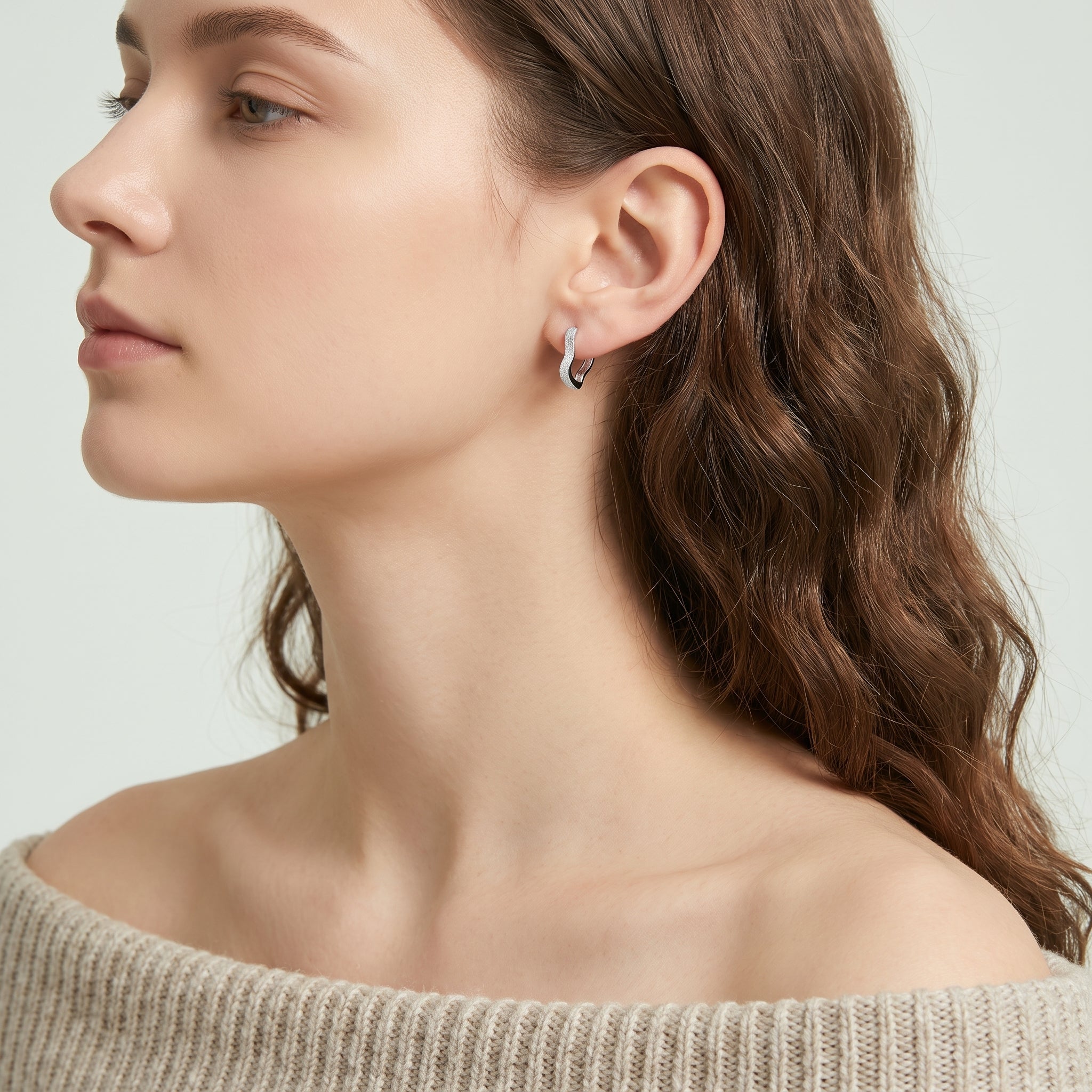 Silver frosted huggie earring in side profile with an oatmeal sweater