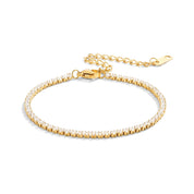 Gold tennis bracelet with small clear crystals on a white background